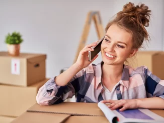 Eine Frau spricht auf ihrem Mobiltelefon, während sie zwischen Umzugskartons steht.