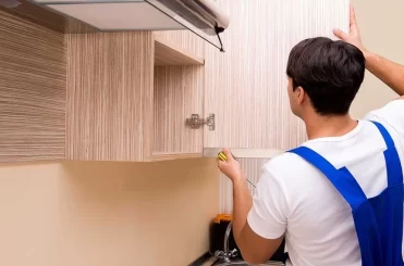 a man in a blue overalls measuring a shelf